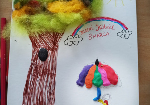 Praca wykonana na Dzień Kobiet z użyciem kolorowej włókniny z której wykonana jest korona drzewa, kredek, mazaków i plasteliny. Widać na nim drzewo, a obok kobietę z parasolem i psem.